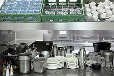 An image of a typical pre-wash table showing stacked dirty dishes and racked cups.