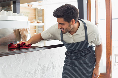 Foodservice cleaning guide. Image of cafe worker cleaning counters.