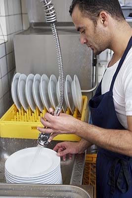 Image of a man pre-scrapping dishes and placing them in a dishmachine rack. 